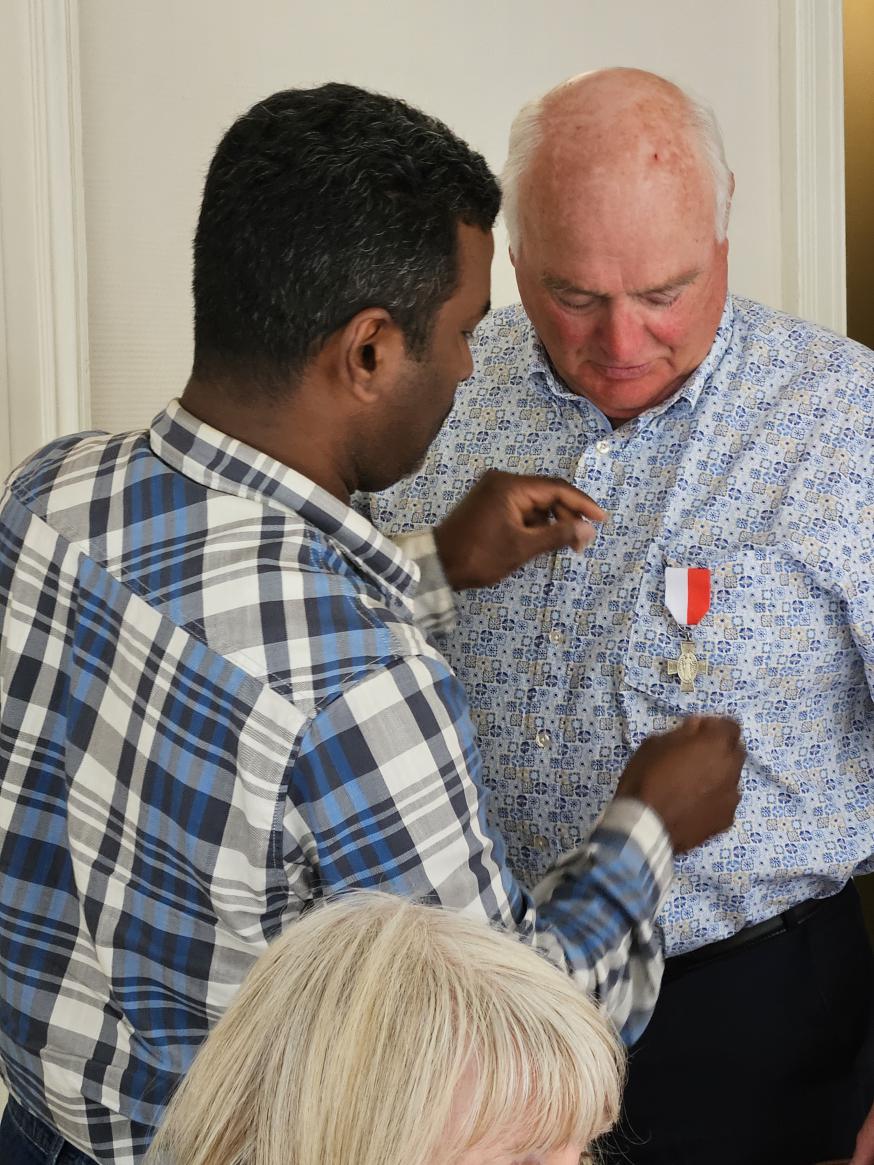 Pater David speldt Vic het zilveren ereteken van verdienste op. © Maria Slegers