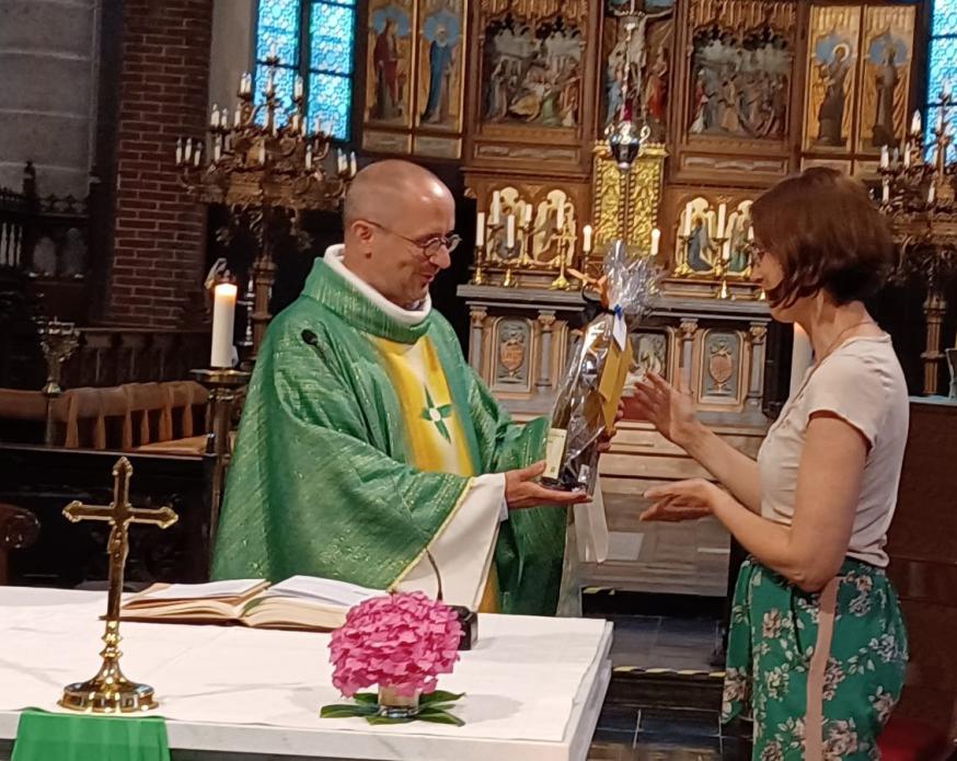 Parochieassistente Lucrèce overhandigt een fles wijn